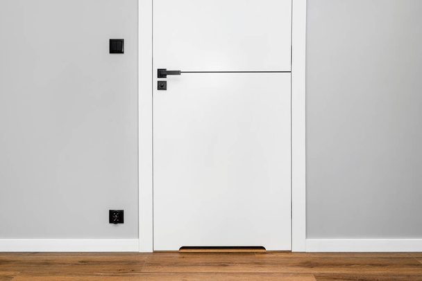 Egy fehér ajtó szellőzéssel alávágva egy matt fekete fogantyúval és egy fekete vonallal középen egy modern házban, vinil panelekkel a padlón.. - Fotó, kép