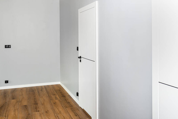 Egy fehér ajtó szellőzéssel alávágva egy matt fekete fogantyúval és egy fekete vonallal középen egy modern házban, vinil panelekkel a padlón.. - Fotó, kép
