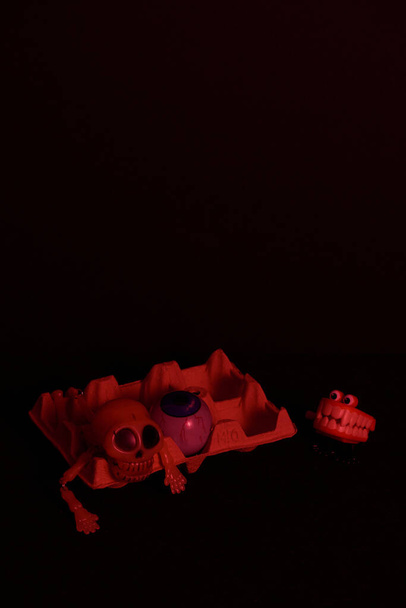 Un cuerpo craneal y un ojo azul ensangrentado en una taza de huevo teñida de rojo sobre un fondo negro - Foto, imagen