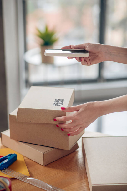 Female with red nails holding her smartphone over a cardboard box - Foto, imagen