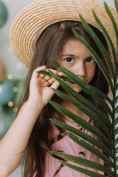 Portrait of cute child girl in pink dress and straw hat with green home plant - Foto, Bild