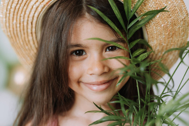 Retrato de niña linda en vestido rosa y sombrero de paja con planta casera verde - Foto, imagen