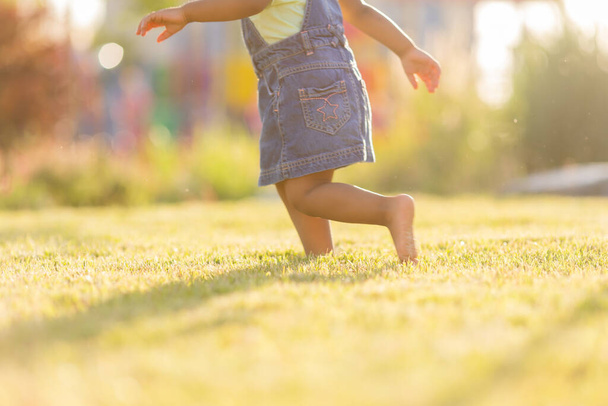Ein kleines dunkelhäutiges Mädchen mit lockigem Haar in Jeans geht an einem sonnigen Tag im Park spazieren. Konzept eines gesunden Lebensstils. Glückliche Kindheit - Foto, Bild