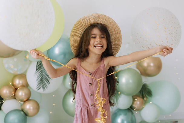 Милая девочка в розовом платье и соломенной шляпе празднование дня рождения, красочные воздушные шары фон - Фото, изображение