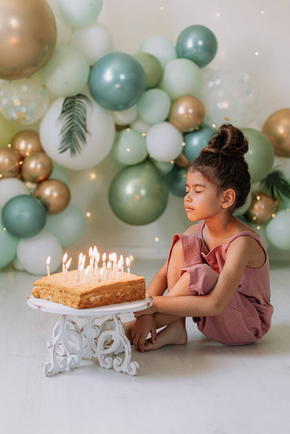 Χαριτωμένο κορίτσι παιδί με τούρτα γενεθλίων στο σπίτι με φόντο μπαλόνια. Γενέθλια παιδιού - Φωτογραφία, εικόνα