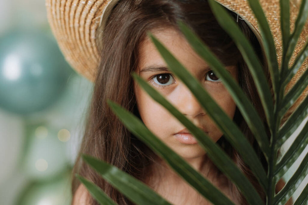 Pembe elbiseli ve yeşil çiçekli hasır şapkalı şirin bir kızın portresi. - Fotoğraf, Görsel