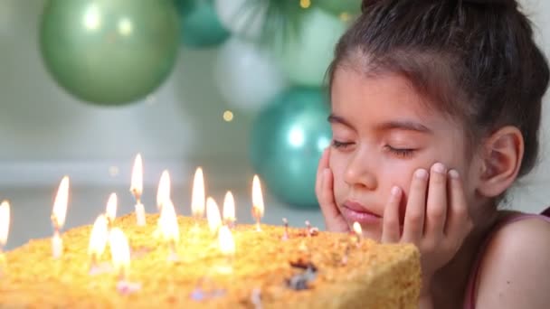 Linda niña con pastel de cumpleaños en casa contra un telón de fondo de globos. Cumpleaños del niño - Metraje, vídeo