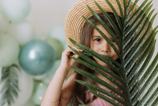 Portré aranyos gyermek lány rózsaszín ruha és szalma kalap zöld otthon növény - Fotó, kép