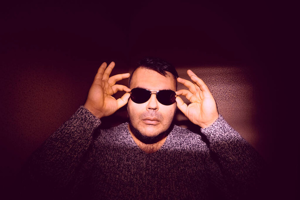 Attractive young man wearing sunglasses and a knitted sweater. looking at the camera. isolated on wall background - Foto, imagen