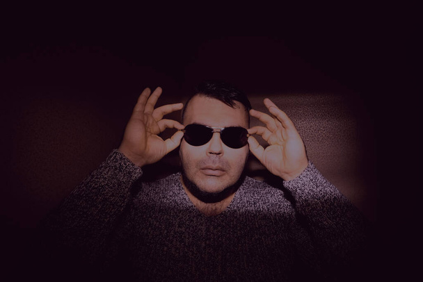 Attractive young man wearing sunglasses and a knitted sweater. looking at the camera. isolated on wall background - Photo, image