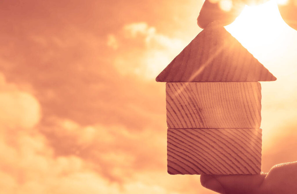 ręka trzymając kawałki drewnianego domu na słonecznym tle nieba. - Zdjęcie, obraz