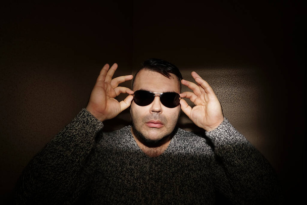 Attractive young man wearing sunglasses and a knitted sweater. looking at the camera. isolated on wall background - Фото, изображение