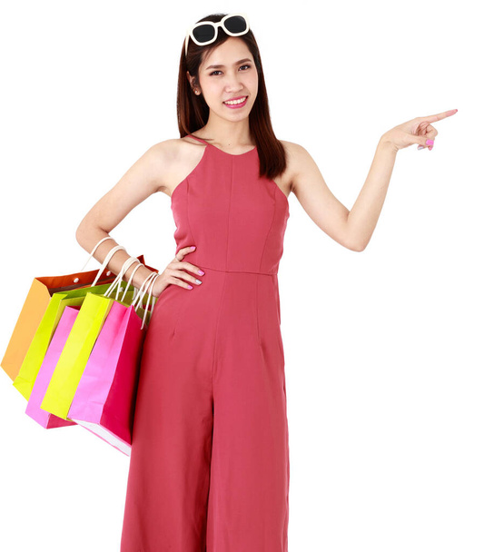 Aasian kaunis hymiö nainen yllään muoti punaiset vaatteet, aurinkolasit, tilalla värikäs paperipussit ostoksille, osoittaa eristetty valkoinen tausta katkaisu mainos. Myynti Alennus käsite - Valokuva, kuva
