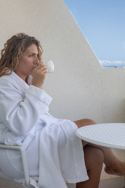 An elegant young caucasian female enjoying a cup of coffee on a balcony - Фото, изображение