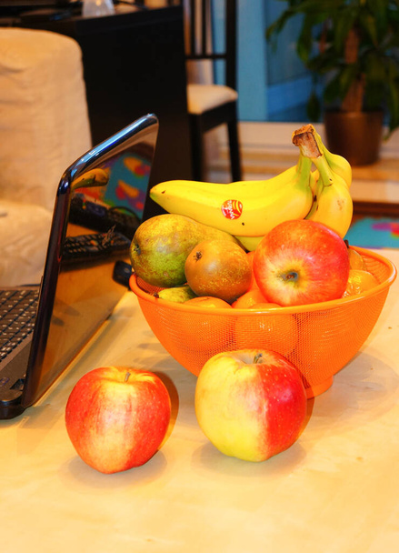 POZNAN, POLAND - Dec 26, 2014: A vertical shot of a laptop with fresh apples, pears and bananas in the orange basket on the table - Fotó, kép