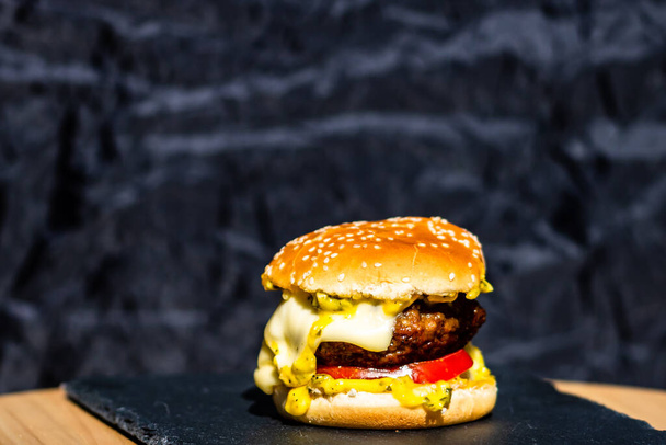 A fresh tasty beef cheeseburger with melted cheese on a black background - Foto, Imagen