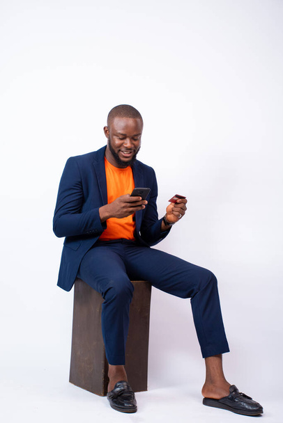 Вертикальный снимок африканского бизнесмена, позирующего с телефоном перед серой стеной - Фото, изображение