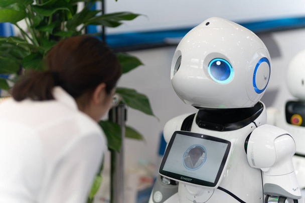 CHONGQING, CHINA - Aug 28, 2019: A soft focus of a Chinese lady interacting with Chinese-made AI robot at a robotics exhibit - Photo, Image