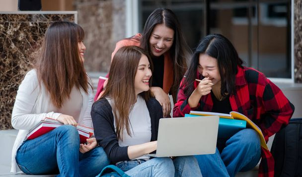 Gruppo di quattro giovani ragazze asiatiche attraenti studenti universitari che studiano insieme utilizzando il computer portatile nel campus universitario all'aperto. Concetto di istruzione, amicizia e vita degli studenti universitari. - Foto, immagini
