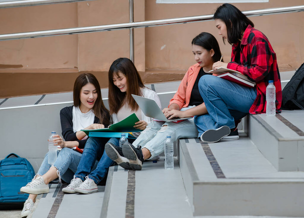 Ομάδα τεσσάρων ελκυστικών Ασιατών φοιτητών που κάθονται κάτω σε κάθε σκάλα στην πανεπιστημιούπολη και σπουδάζουν σε εξωτερικούς χώρους. Έννοια για την εκπαίδευση, τη φιλία και τη ζωή των φοιτητών. - Φωτογραφία, εικόνα