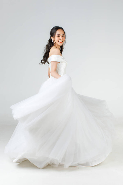 Full length of young attractive Asian woman, soon to be bride, wearing white wedding gown looking happy spinning. Concept for pre wedding photography. - Fotografie, Obrázek