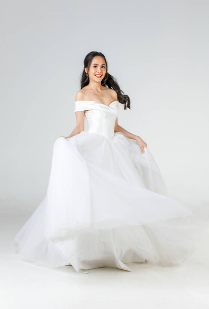Full length of young attractive Asian woman, soon to be bride, wearing white wedding gown looking happy spinning. Concept for pre wedding photography. - Foto, Imagem
