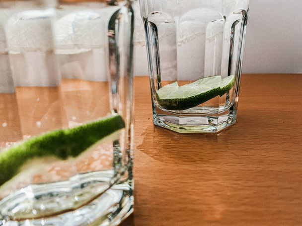 A close-up shot of lime water in glass cups on a wooden table in the kitchen - Фото, зображення
