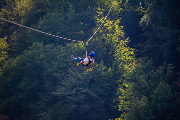 Fun, adrénaline et aventure sur la tyrolienne. Adolescent s'amusant sur une tyrolienne sur fond de forêt panoramique. Zipline dans la forêt. Les gens obtiennent l'adrénaline par la tyrolienne dans la forêt - Photo, image