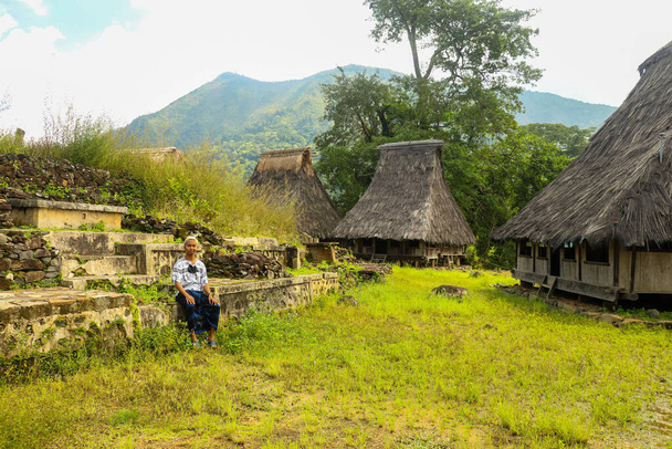 a young man with sarong sitting onthe edge central stone elevated area in the center of the Wologai village near Kelimutu in East Nusa Tenggara - Photo, Image