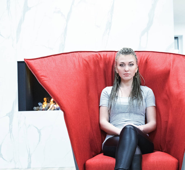 vaguely evil-looking girl waits in a slightly creepy red armchair - Photo, Image