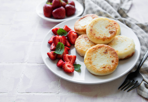 Quark-Pfannkuchen, Ricotta-Krapfen auf Keramikteller mit frischen Erdbeeren. Gesundes und leckeres Frühstück am Morgen. Grauer Betonhintergrund. - Foto, Bild