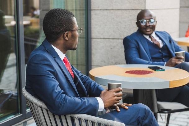 Meeting of two long-time friends of black African American businessman in suits outdoors in a summer city cafe - 写真・画像