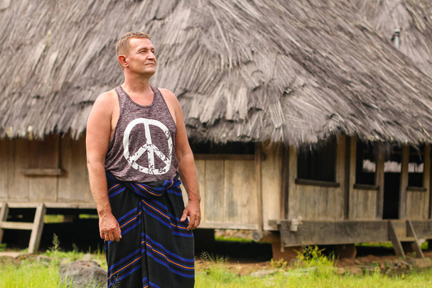 caucasian wearing traditional sarong standing the front of traditional house in Wologai village East Nusa Tenggara - Foto, Imagen