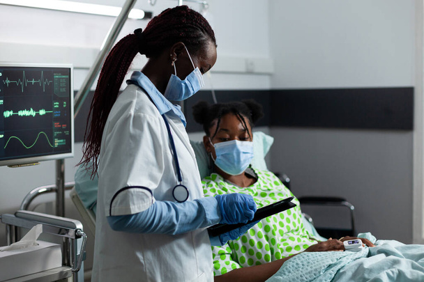 Afrikalı etnik kökenli doktor klinikteki hasta hastaya yardım ediyor - Fotoğraf, Görsel