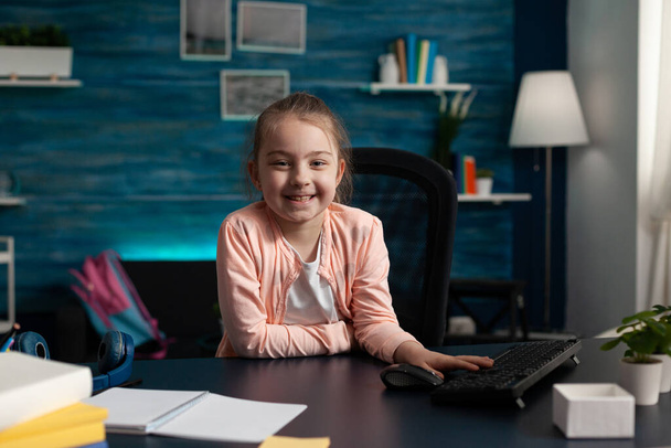 Retrato de uma criança em idade escolar sorridente sentada à mesa na sala de estar - Foto, Imagem