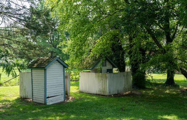 Два старых туалета под большими старыми деревьями в школе. - Фото, изображение