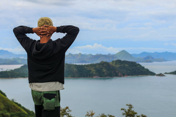Ritratto di giovane sulla cima della collina con giacca nera sullo sfondo del mare a Labuan Bajo. - Foto, immagini