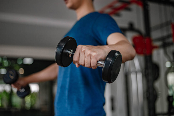Training gym concept een jonge volwassene met behulp van zijn gespierde sterke arm tilt een halter omhoog en omlaag in de sportschool. - Foto, afbeelding