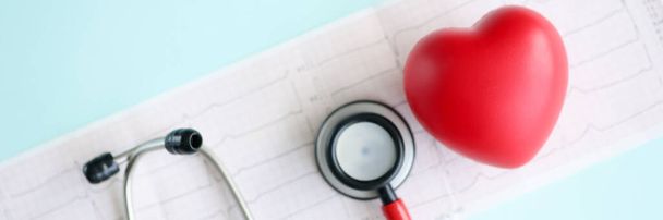 Rode speelgoed hart en stethoscoop liggen op cardiogram closeup - Foto, afbeelding