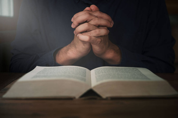 O homem está lendo e orando a escritura ou Bíblia sagrada em uma mesa de madeira com espaço de cópia. Religião, acredite Conceito. - Foto, Imagem