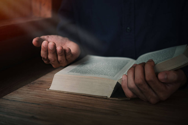 Człowiek czyta i modli się Pismo Święte lub świętą Biblię na drewnianym stole z przestrzenią do kopiowania. Religia, uwierz Koncepcja. - Zdjęcie, obraz