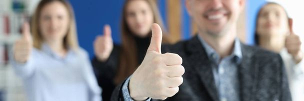 Succesvolle jonge zakenman tonen duim tegen de achtergrond van collega 's closeup - Foto, afbeelding