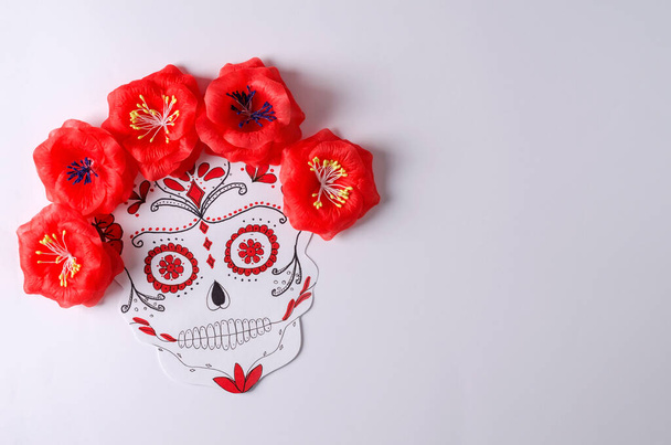 Traditional sugar skull for the Mexican holiday Dia de Muerto with red flowers on a white background, flat layout copying space - Photo, Image