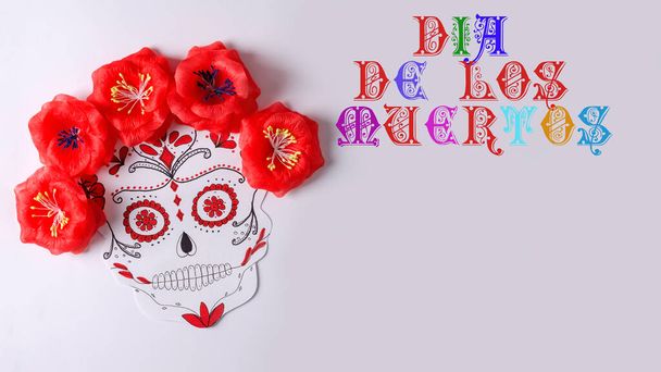 Традиционный сахарный череп для мексиканского праздника Dia de Muerto с красными цветами на белом фоне с надписью Dia de Los Muertos, копировальное пространство - Фото, изображение