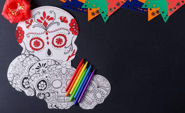 Przygotowanie do meksykańskiego święta Dia de los Muertos. Rysunek maski Katriny na czarnym tle, z kolorowymi ołówkami i flagami, płaski układ - Zdjęcie, obraz