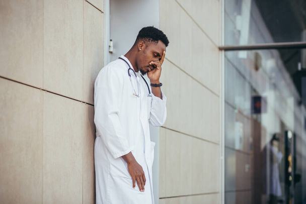 male doctor at the clinic holding his head has health problems and tired after a hard day, depressed did not get the desired result, afro american doctor is sad - Foto, immagini