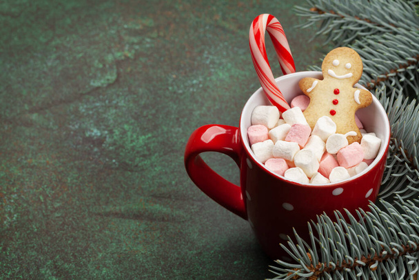 Tarjeta de felicitación navideña con abeto, caja de regalo y taza de cacao con malvavisco, bastón de caramelo y jengibre. Sobre fondo de piedra con espacio de copia para tus saludos de Navidad - Foto, imagen