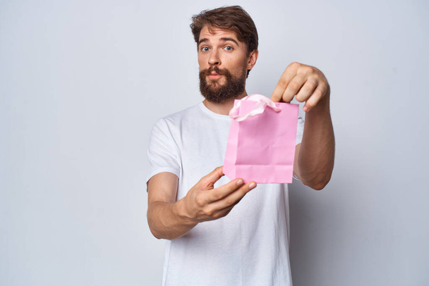 Cheerful bearded man with pink small package gift light background - Photo, image
