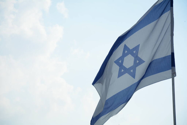 Israeli flag weaving in the wind against bright skies - Foto, imagen