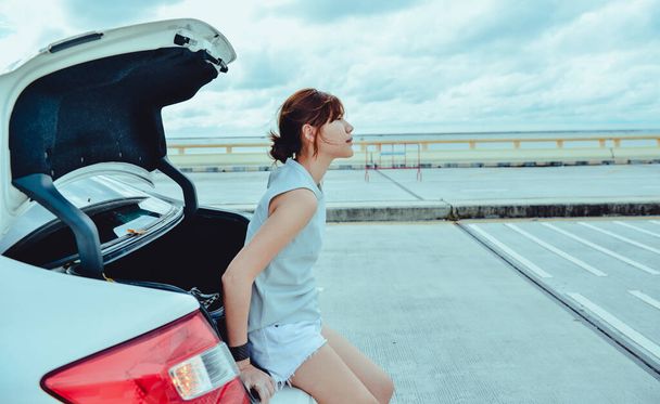 Asian Woman traveler sitting on hatchback car with sky and road background - Фото, изображение